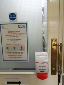 hand sanitiser on door with NHS covid 19 advice poster