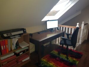 Computer on desk with chair in front of slanted skylight