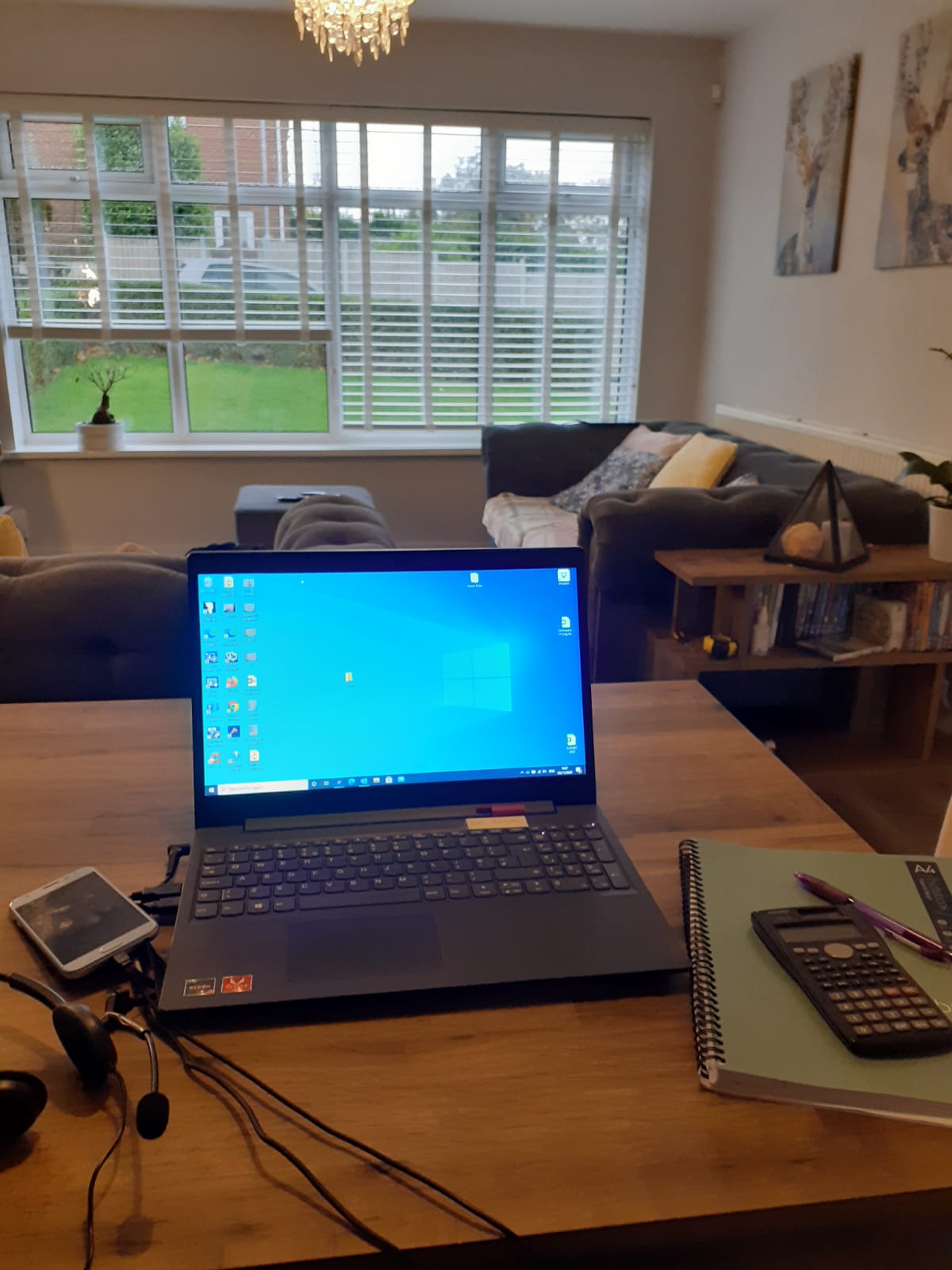 Laptop, notebook and calculator on table in front of sofas and window