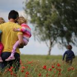 Man carries two children through meadow, while other runs ahead