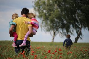 Man carries two children through meadow, while other runs ahead