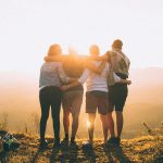four-person-standing-on-cliff-in-front-of-sun